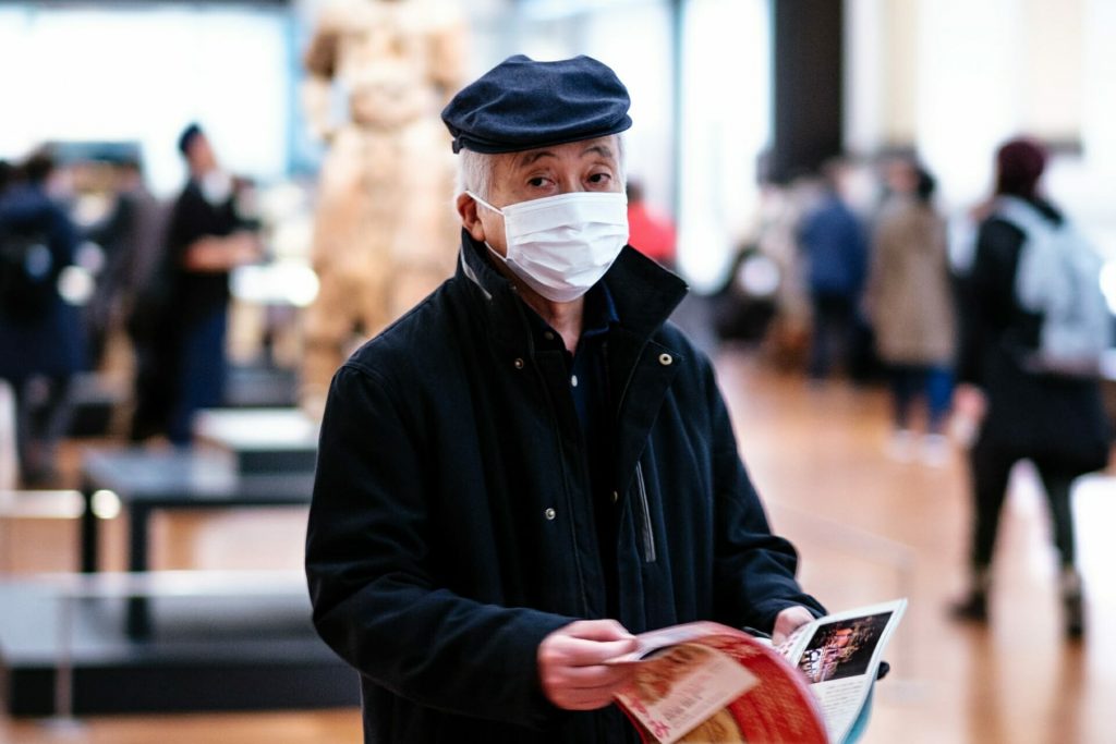 An old man wearing face mask and holding a magazine